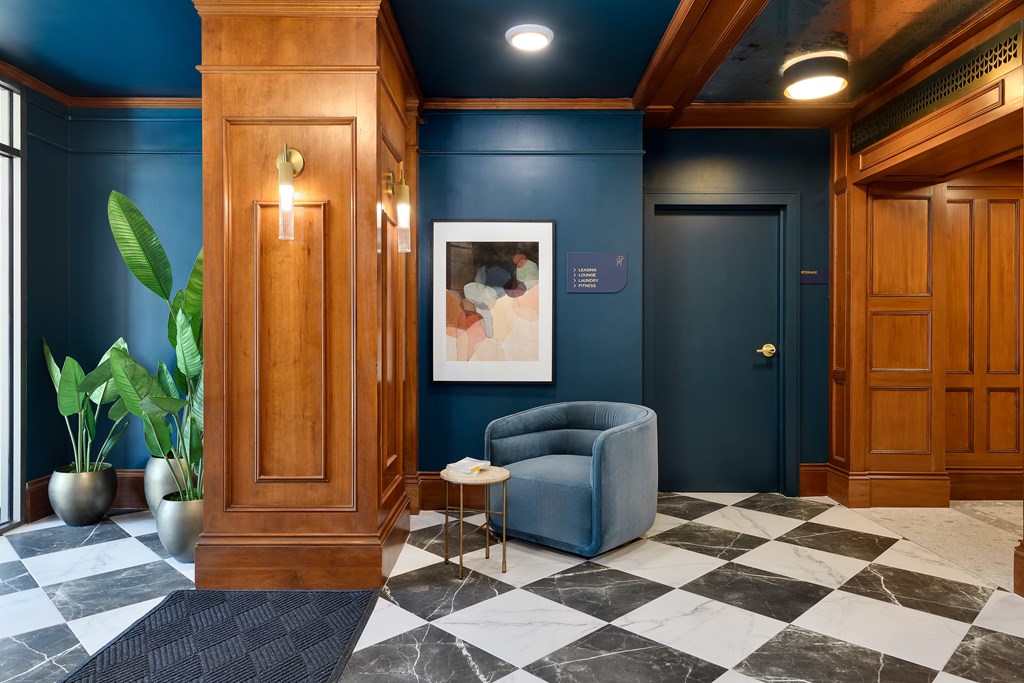 Apartment lobby with blue walls, wood paneling, and a blue velvet chair.