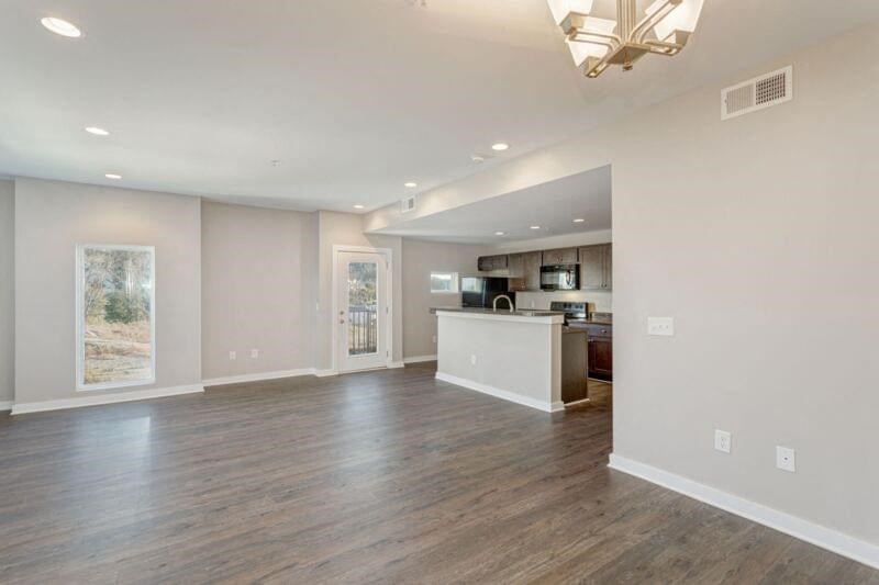 an empty living room with a kitchen in the background