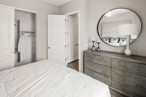 A white bedroom with a round mirror and a dresser.