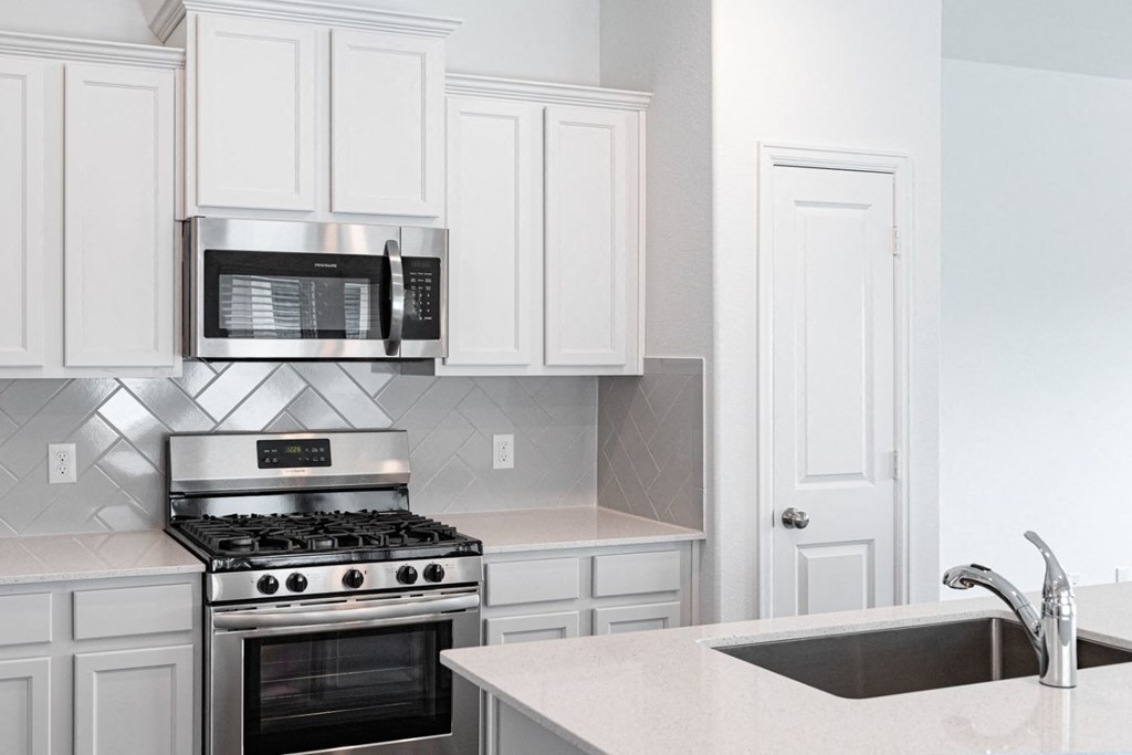 Houses in Humble, TX for Rent - Edgewater at the Lagoon - Kitchen with White Cabinets, Stainless Steel Appliances, Quartz Countertops, and Tile Backsplash