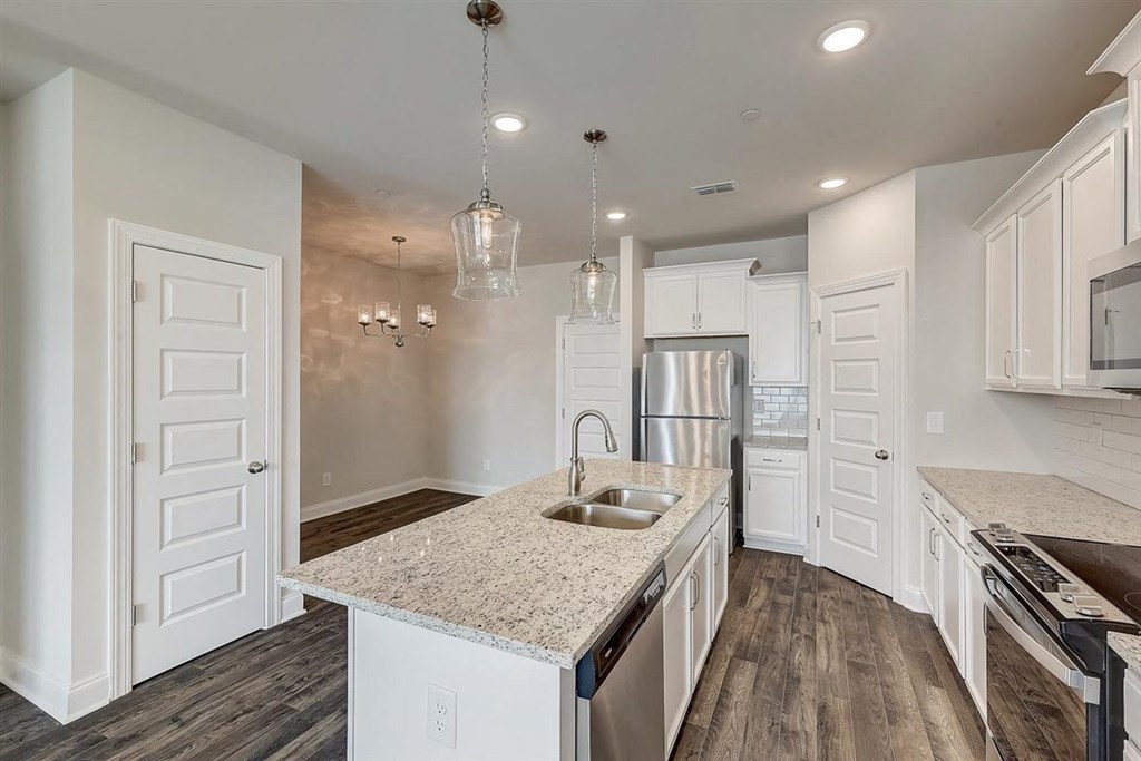 Gallatin, TN, Apartments - The Gardens at Preston Park - Modern Kitchen with Vinyl Plank Flooring, Quartz Countertops, White Cabinetry, Stainless Steel Appliances, Tile Backsplash, Large Island, and Pendant Lights.