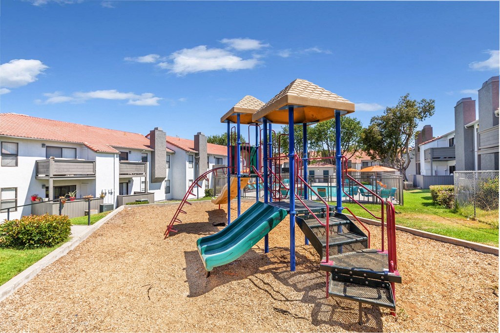 Apartments For Rent In Moreno Valley, CA - Sorelle Apartments - Playground with Slide Towers and View of Pool and Apartment Buildings.