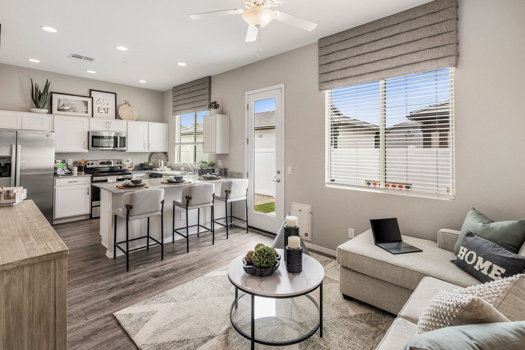 A modern kitchen with a dining table and chairs, a laptop on a sofa, and a coffee table in the center.