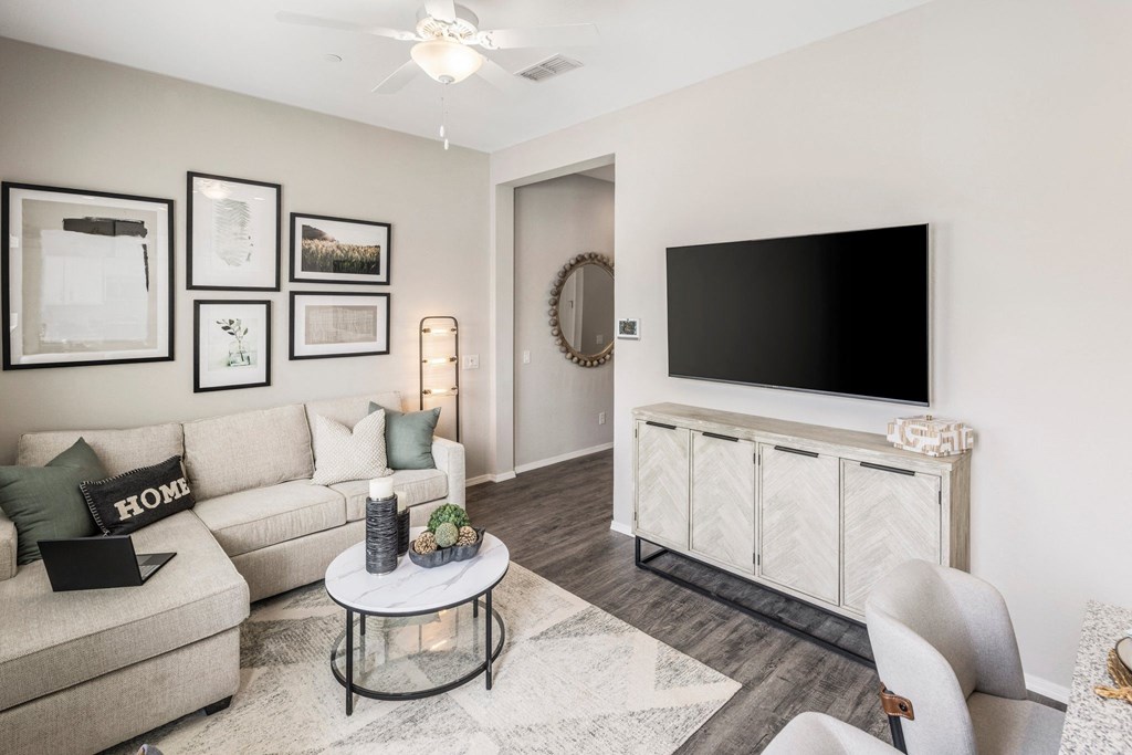 A living room with a grey sofa, a white coffee table, a black television and a mirror on the wall.