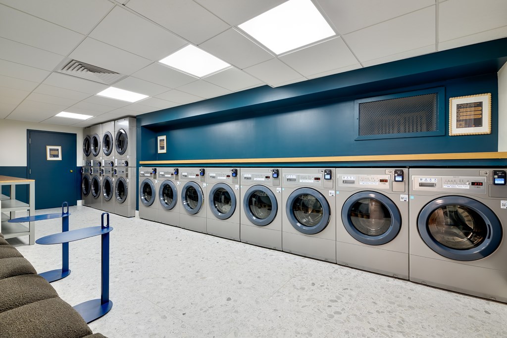 Modern laundromat with rows of silver washing machines, blue accent wall, and seating area.