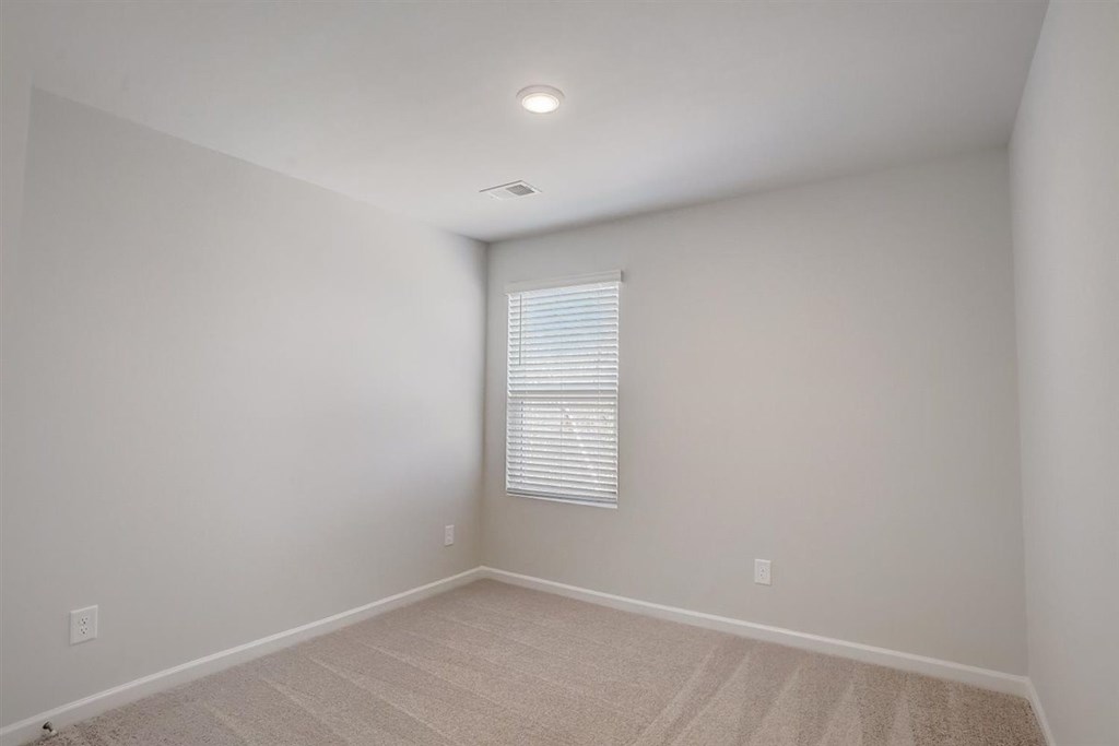 A room with a window covered by blinds and a carpet on the floor.