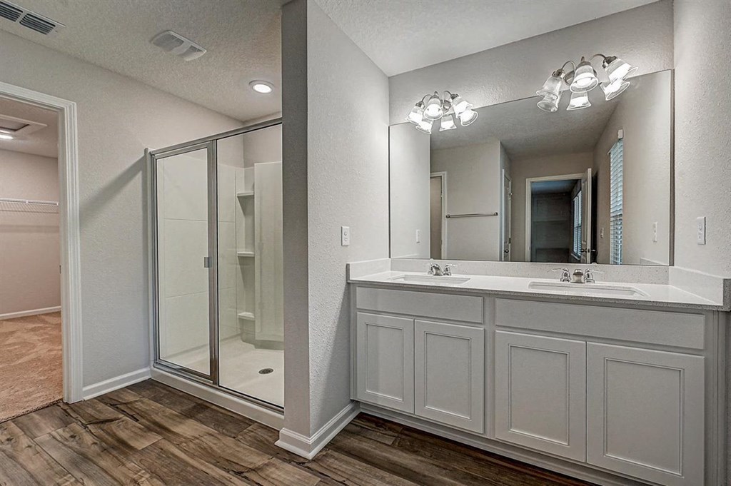 Modern bathroom with double vanity, glass shower, and wood-look flooring.