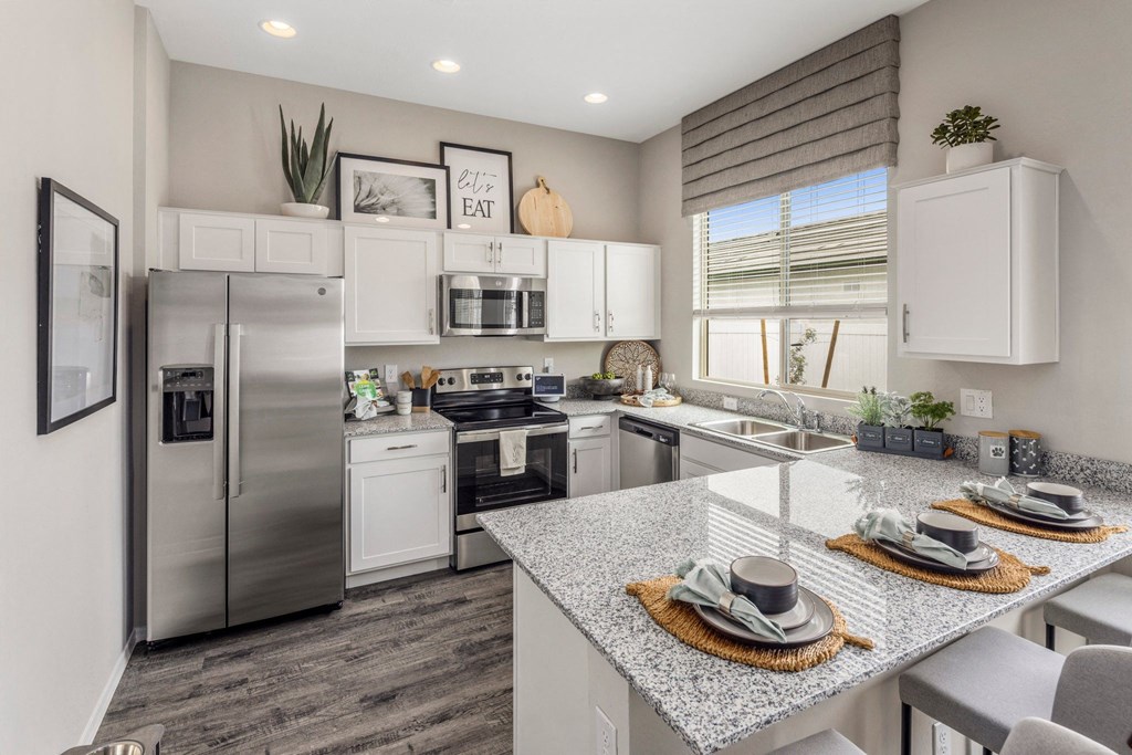 Phoenix AZ Apartments for Rent - The Crofton at Sheely Farms - Modern Kitchen with Stainless Steel Appliances, Granite Countertops, White Cabinetry, Dual Sink, Chairs, and a Nearby Window