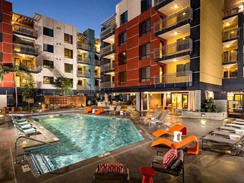 Long Beach, CA, Apartments with In-Unit Washer and Dryer - Urban Village -  Swimming Pool Surrounded by Lounge Seating, and Multi-Story Residential Buildings.