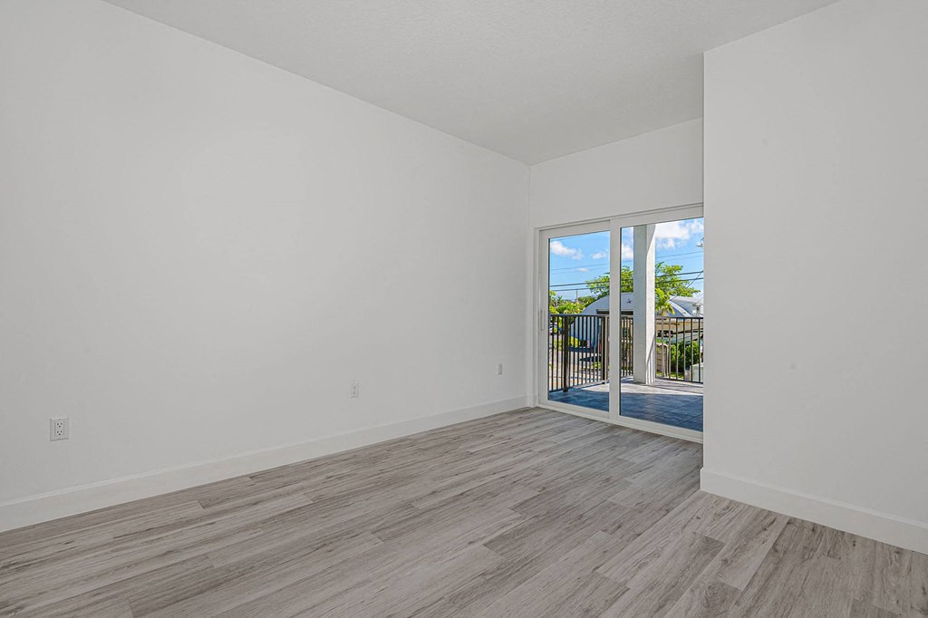 Pearl at Pompano Beach Townhomes in Pompano Beach, FL bedroom with gray wood floors, white walls, and sliding glass doors to a balcony.