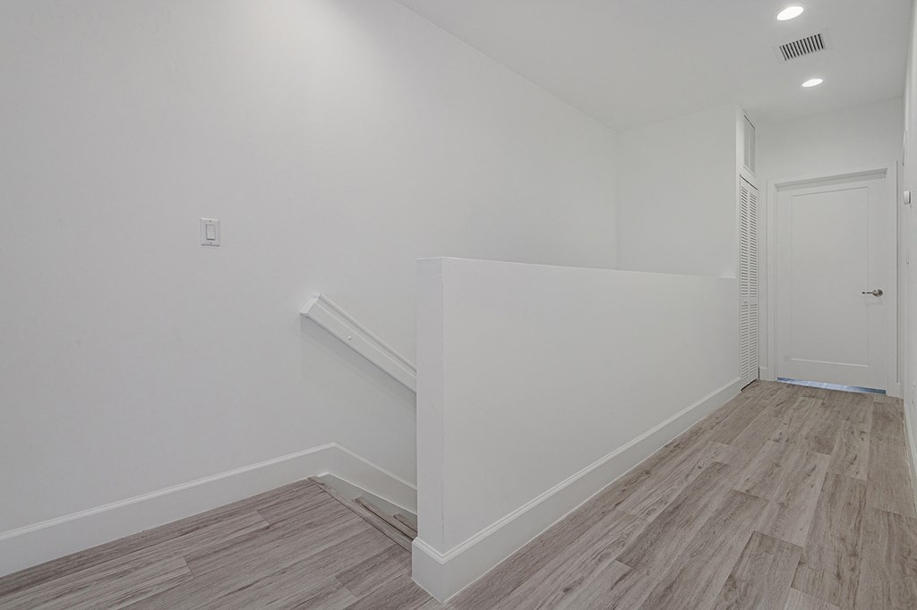 Pearl at Pompano Beach Townhomes in Pompano Beach, FL Bright white hallway with wood-look flooring, stairs, and a closed door.