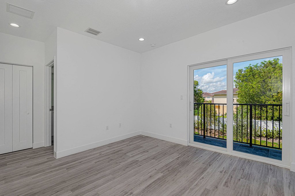 Pearl at Pompano Beach Townhomes in Pompano Beach, FLbedroom with gray wood floors, white walls, sliding glass door to balcony.