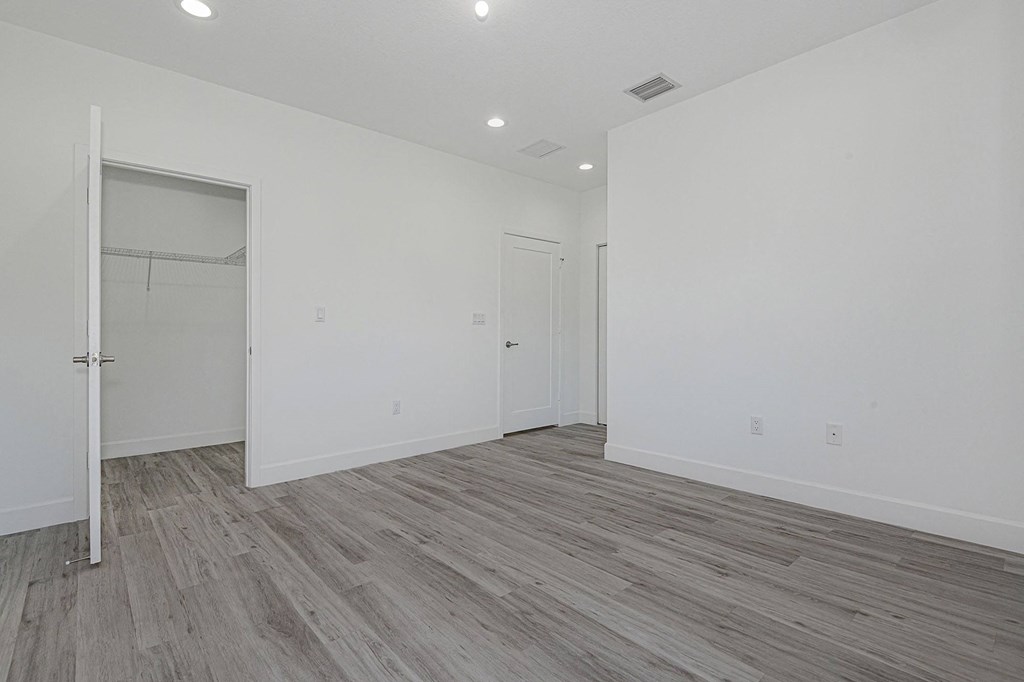 Pearl at Pompano Beach Townhomes in Pompano Beach, FL Empty bedroom with white walls, gray wood-look flooring, and open closet.