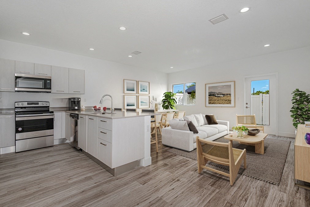 Open-concept kitchen and living room with stainless steel appliances, white cabinets, wood floors, and modern furniture.