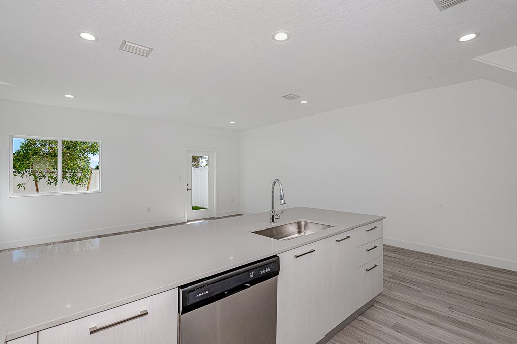 Modern kitchen with white cabinets, quartz countertop island, and stainless steel dishwasher.