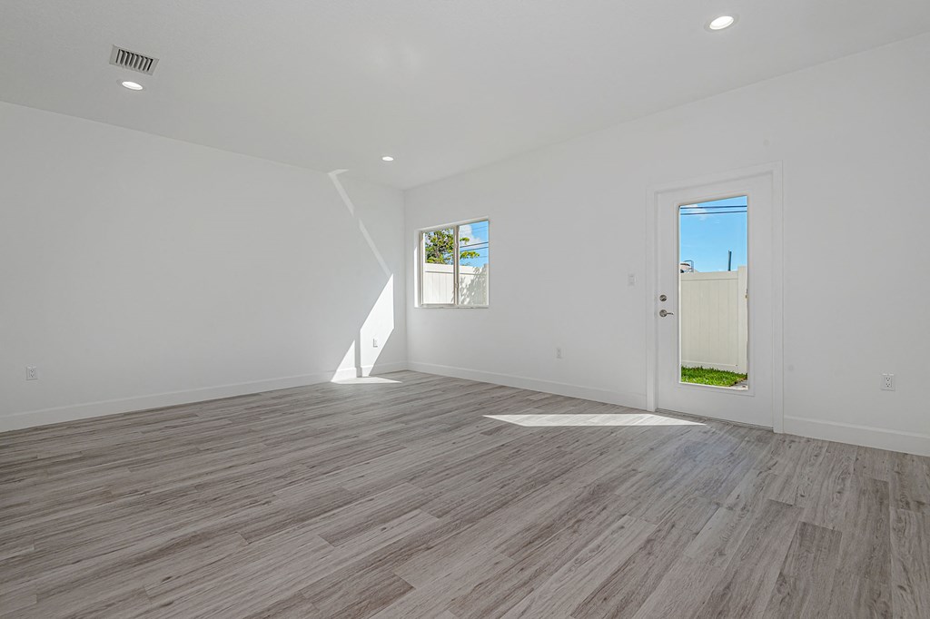 Pearl at Pompano Beach Townhomes in Pompano Beach, FL bright room with gray wood-look flooring, white walls, window, and glass door to backyard.