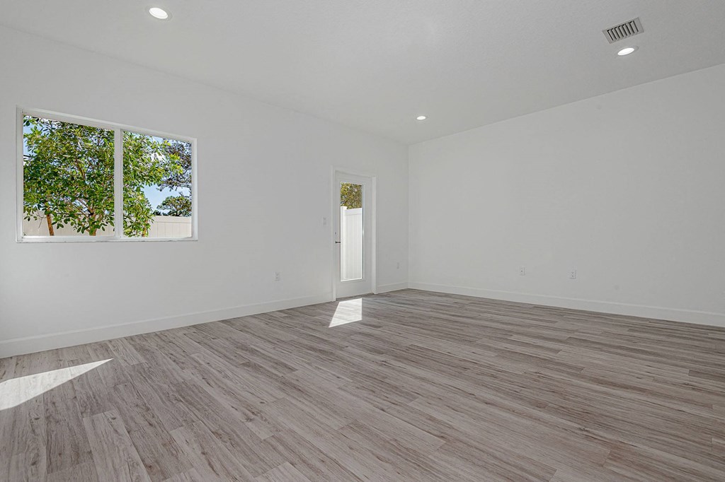 Pearl at Pompano Beach Townhomes in Pompano Beach, FL livingroom with white walls, wood-look flooring, window, and glass door.