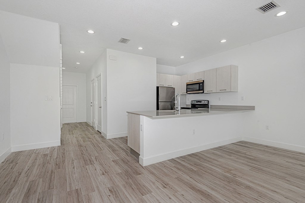 Modern apartment interior with white walls, wood-look flooring, and an open kitchen.