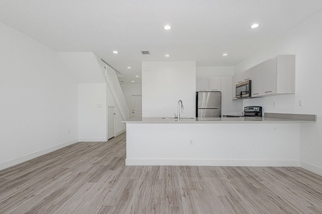 Open-concept kitchen and living area with white walls, wood-look flooring, and stainless steel appliances.