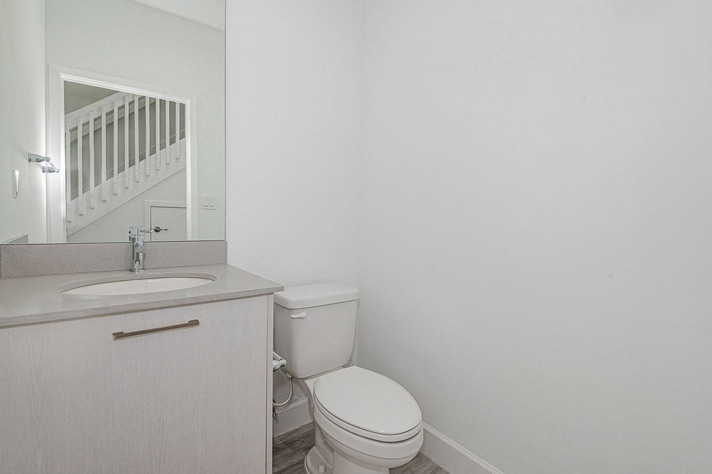 Pearl at Pompano Beach Townhomes in Pompano Beach, FL Modern powder room with white walls, toilet, and vanity with a mirror reflecting a staircase.