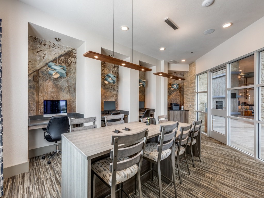 A modern office space with a long table and chairs, a brick wall, and a glass door leading to another room.