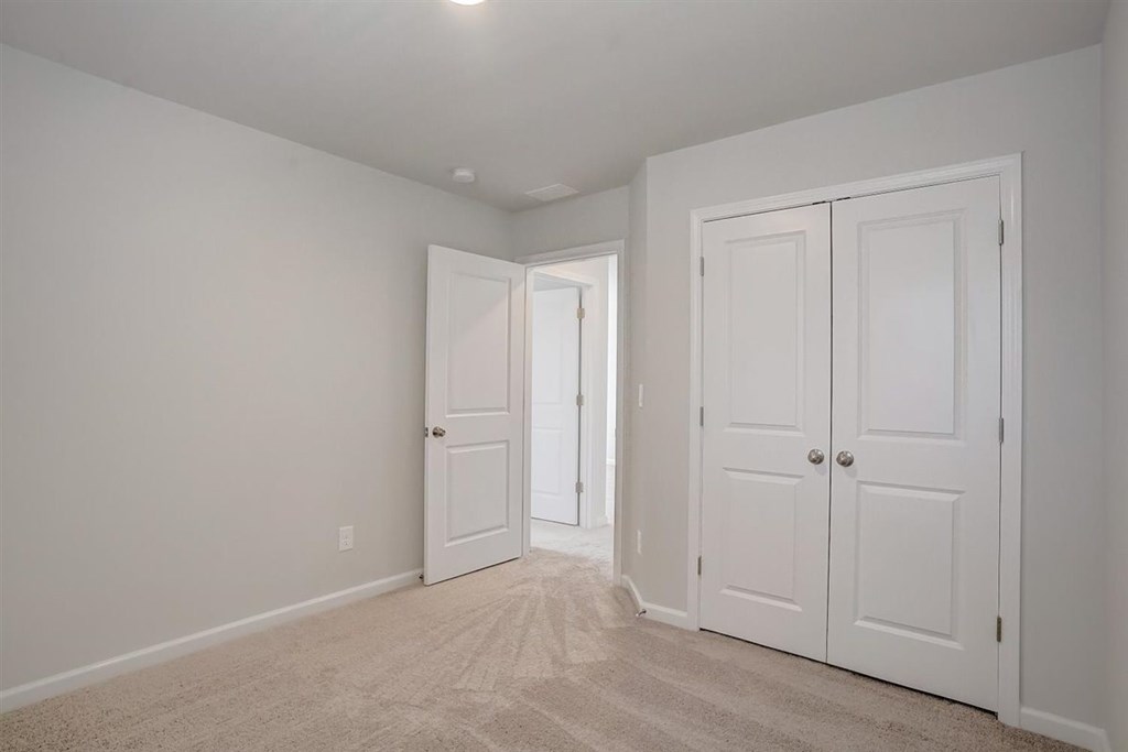 A room with white walls and carpeted floor with two white doors.