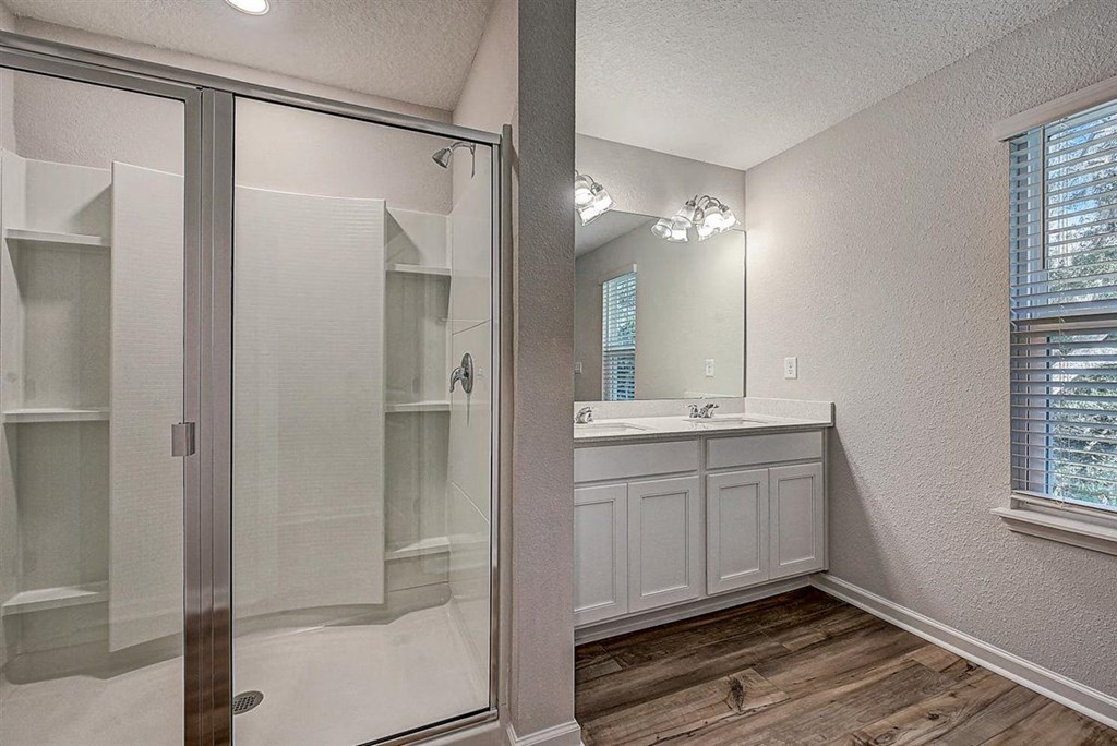 Modern bathroom with glass-enclosed shower, double vanity, and wood-look flooring.