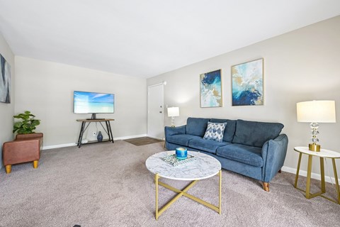 A living room with a blue couch, a coffee table, and a painting on the wall.