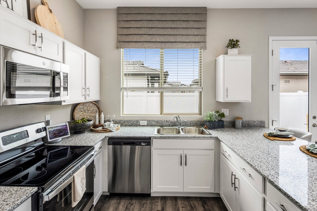 Phoenix AZ Apartments for Rent - The Crofton at Sheely Farms - Modern Kitchen with Stainless Steel Appliances, Granite Countertops, White Cabinetry, Dual Sink, Chairs, and a Nearby Window