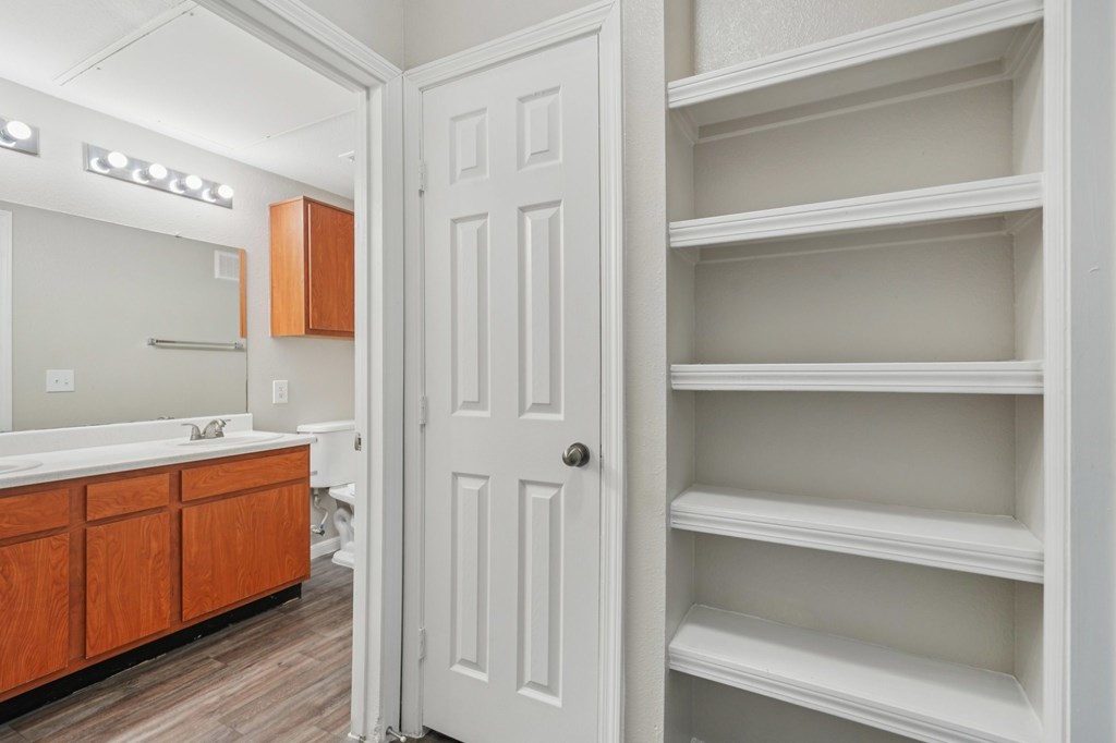 A white door is open to a room with a white sink and wooden cabinets.