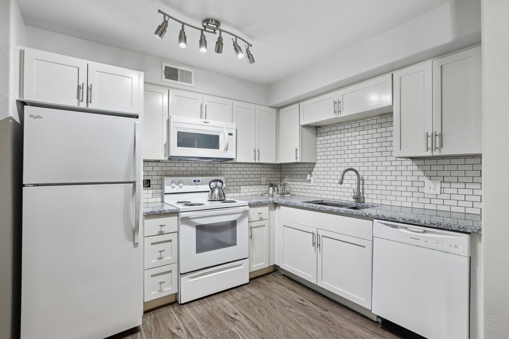 A white kitchen with a refrigerator, microwave, oven, and sink.