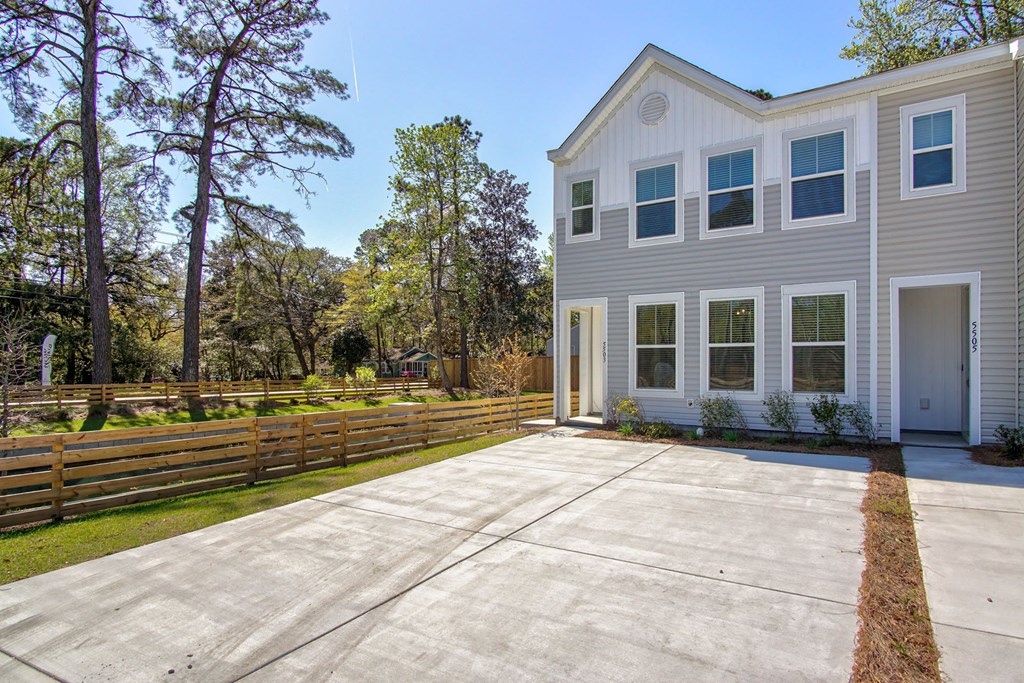 Pet-Friendly Homes for Rent in North Charleston, SC - Sumner Village - Front Exterior of Apartment Home with Driveway, Wooden Fence, and View of Trees and Bushes.