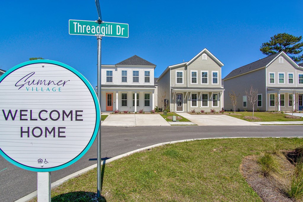 Houses for Rent in North Charleston, SC - Sumner Village - Street View of Apartment Homes with Driveways, Sidewalk, Manicured Lawns, and Property Signage.