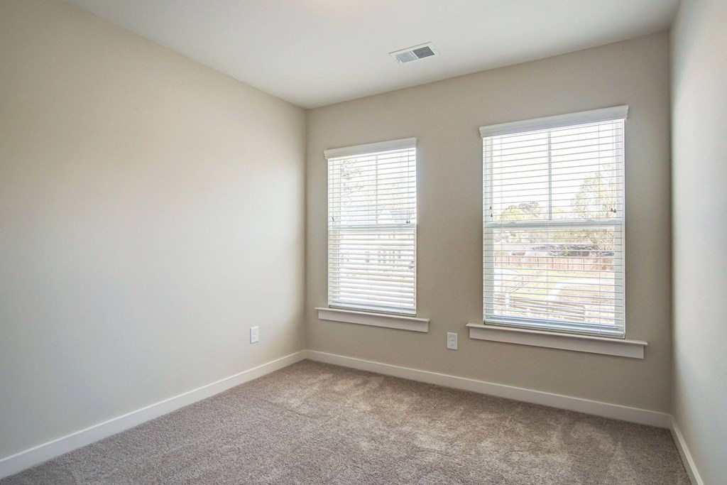 an empty room with two windows and a carpeted floor