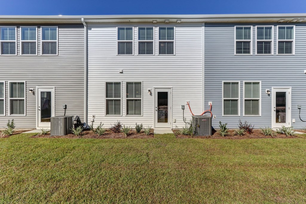 North Charleston, SC Townhomes Near The Citadel - Highland Townhomes - Exterior View of Townhomes with White and Grey Walls, and Backyards with Manicured Grass Lawns.