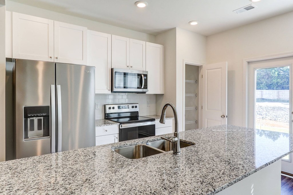 North Charleston, SC Townhomes Near The Citadel - Highland Townhomes - Kitchen With Stainless Steel Appliances, White Cabinets, White Tile Backsplash, White Walls, and Granite Countertops