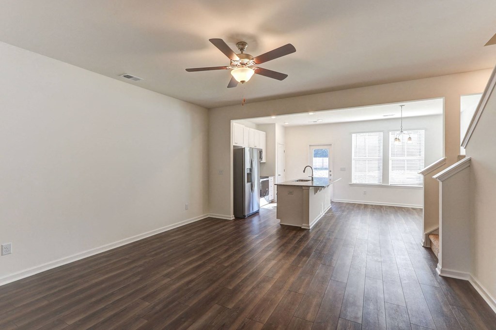 an empty living room with a ceiling fan and a kitchen
