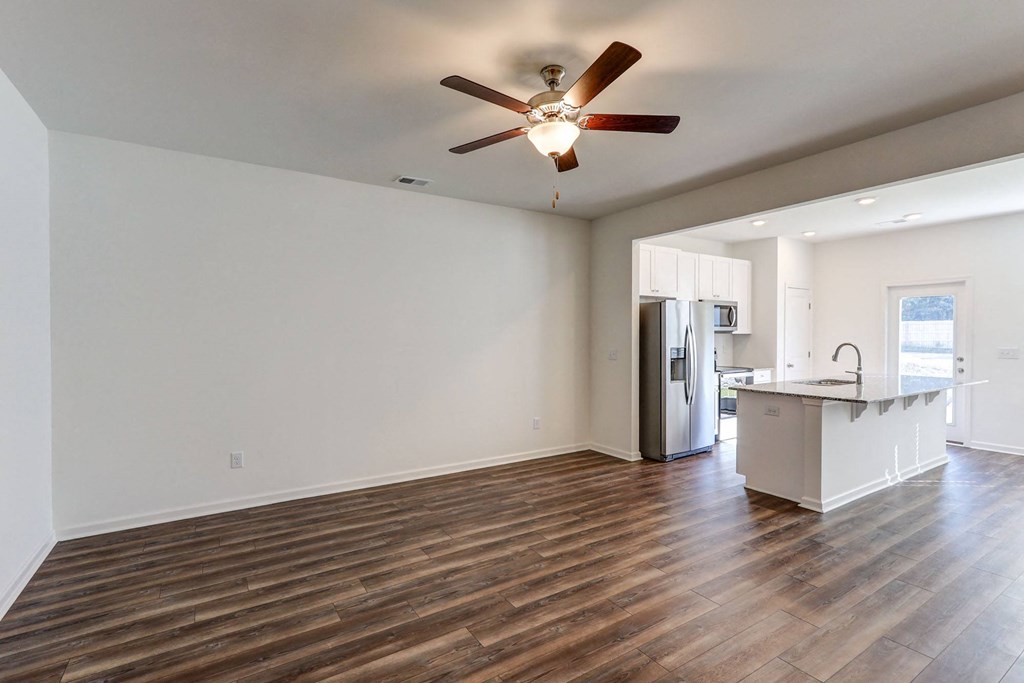 an empty living room with a kitchen and a ceiling fan