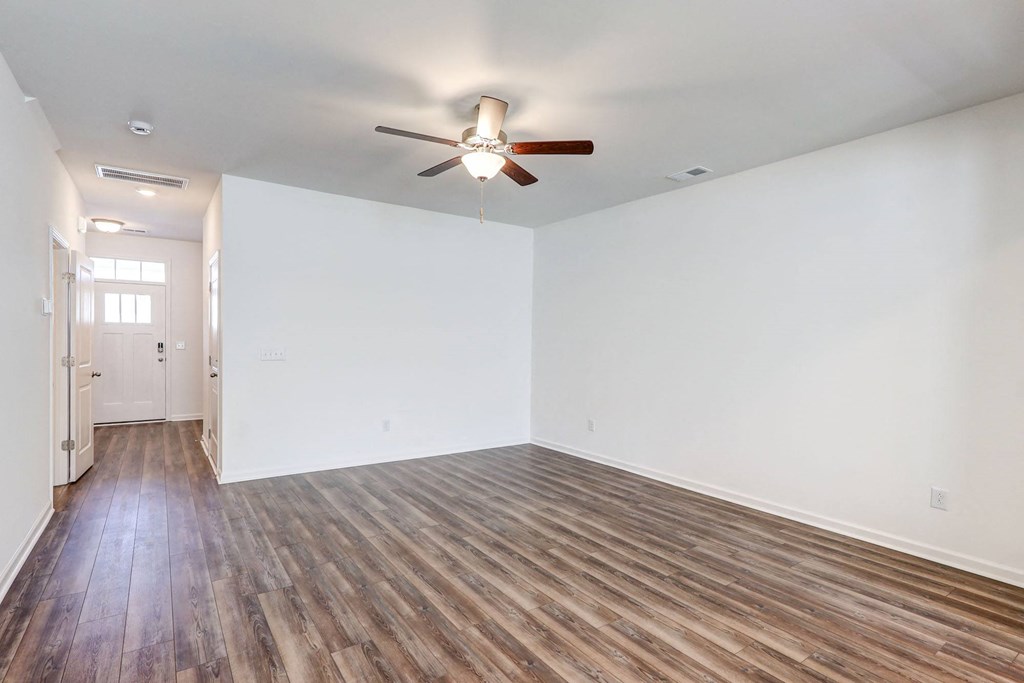 Four-BR Townhomes in North Charleston, SC - Highland Townhomes - Empty Living Room With White Walls, Wood-Style Flooring, and A Ceiling Fan