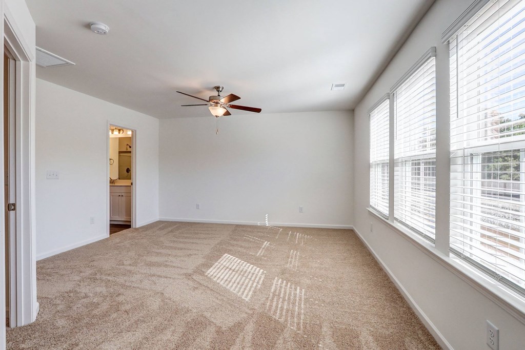 an empty living room with large windows and a ceiling fan