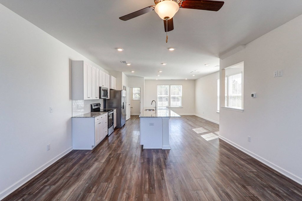 an empty living room with a ceiling fan and a kitchen
