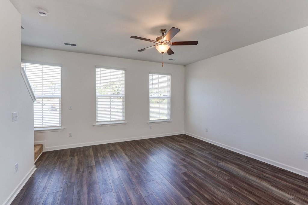 Townhouses for Rent in North Charleston, SC - Highland Townhomes - Empty Living Room with Hardwood Floor, Multiple Windows, White Walls, and Ceiling Fan.