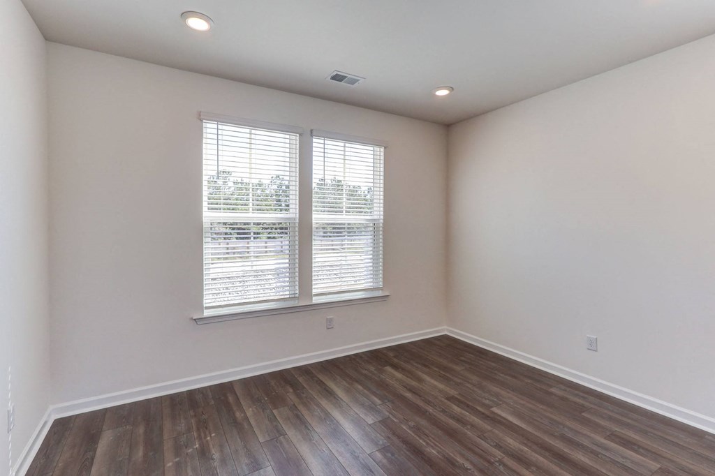 an empty living room with wood flooring and two windows