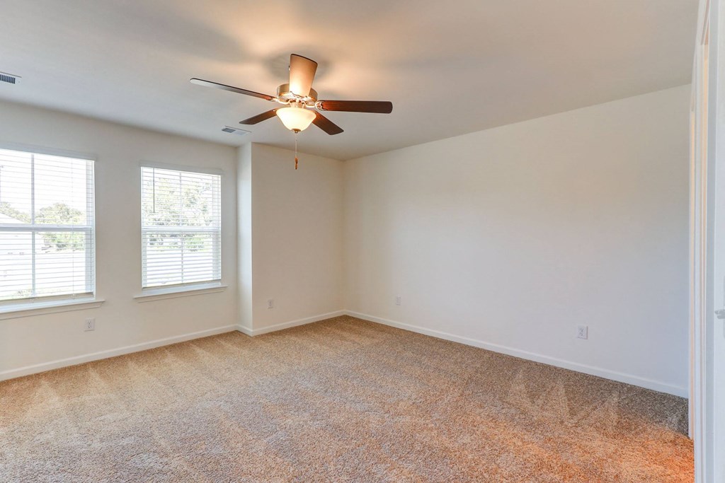 an empty living room with a ceiling fan and two windows