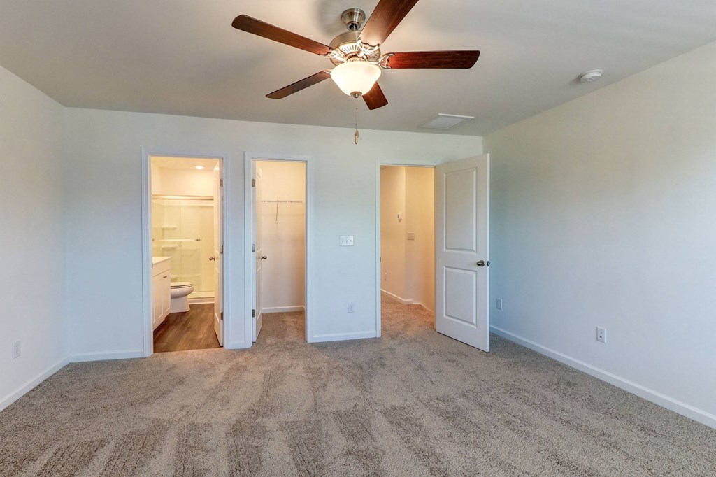 an empty living room with a ceiling fan and a door to a bathroom