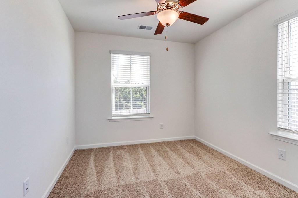 an empty room with a ceiling fan and two windows