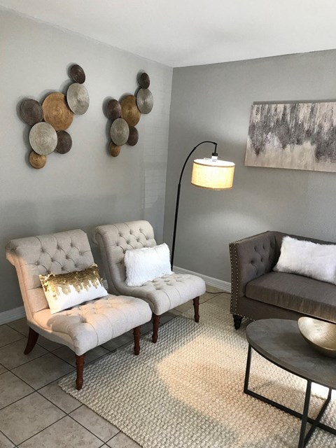 A grey couch sits in a living room with a lamp and a painting on the wall.