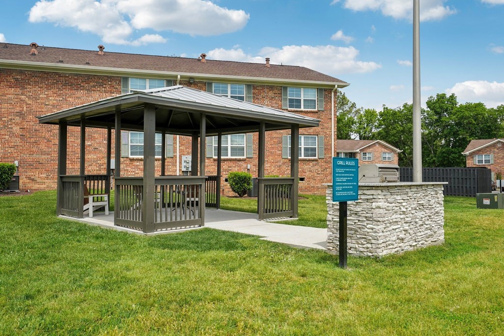 Apartment complex grilling area with gazebo, grill, and grill rules sign.