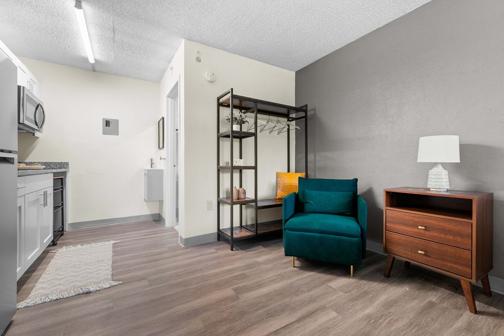 a living room with a blue chair and a kitchen with a stove and a microwave