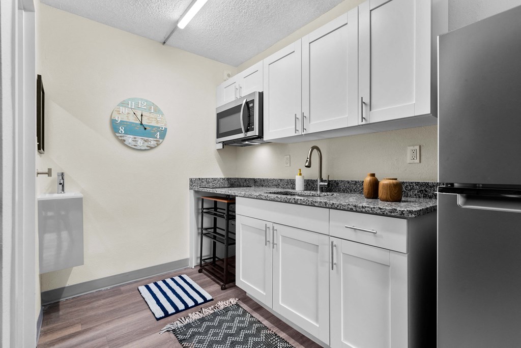 an open kitchen with white cabinets and a counter top with a sink and a refrigerator
